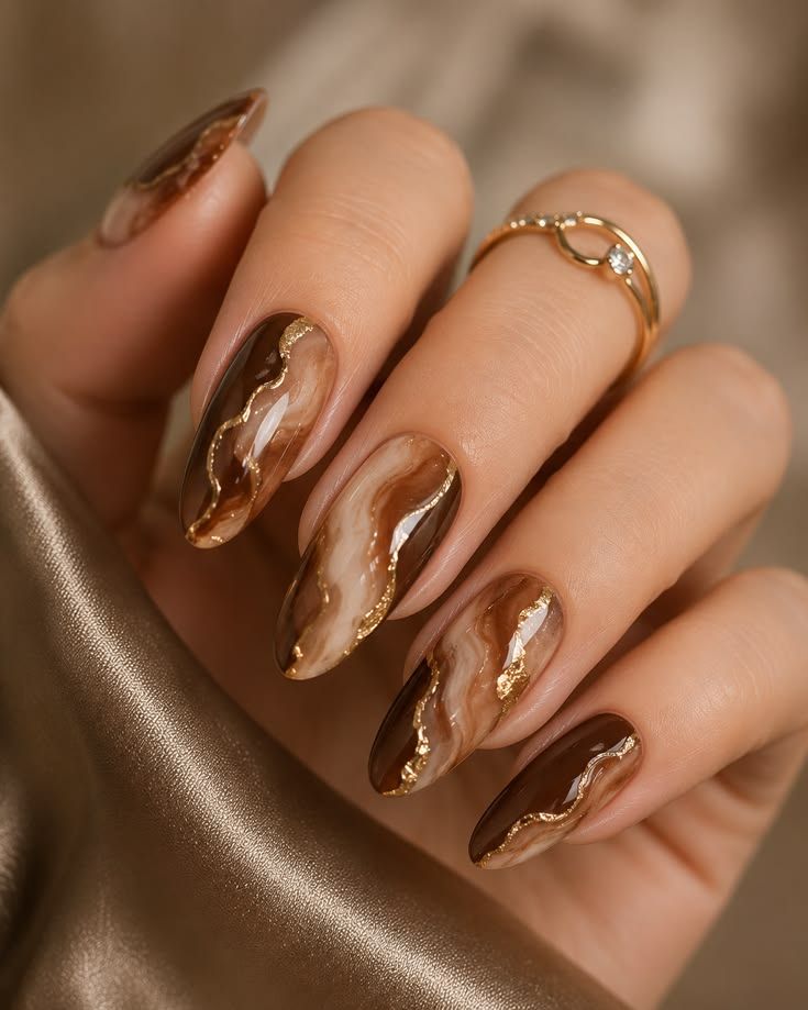 Brown marble almond nails with gold veins on silk, marble with metallic gold lines on fabric