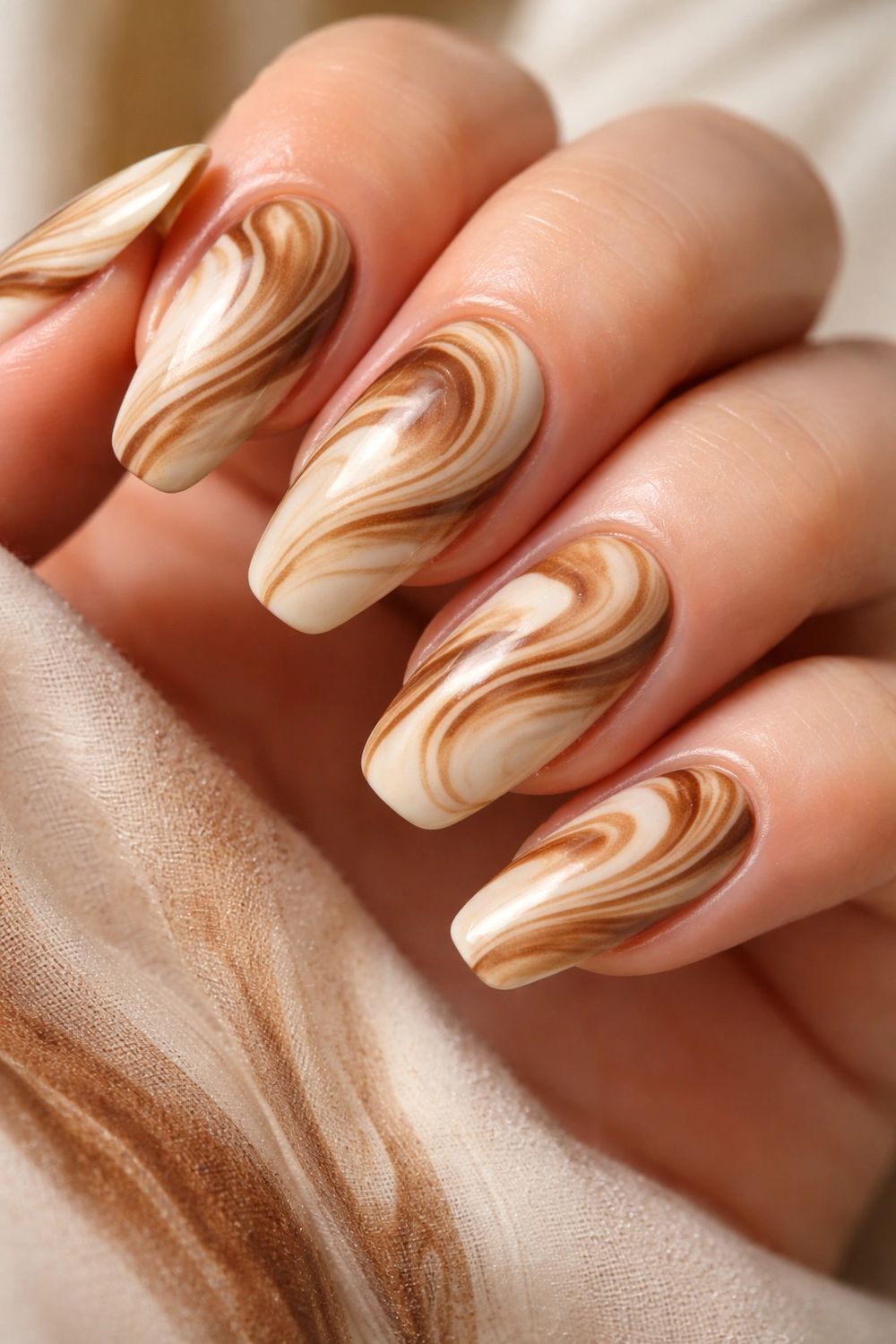 Latte swirl marble almond nails on wood, cream and caramel swirls styled on a table