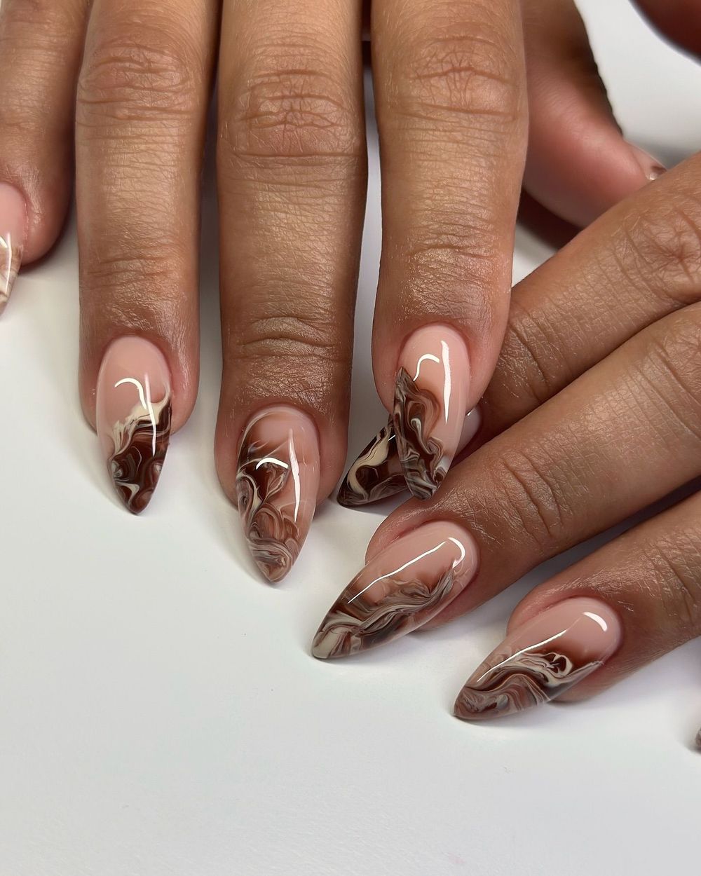 Marble French almond nails on brown skin, marble tips over a bare base on warm skin