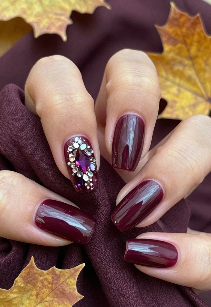 Burgundy almond nails with a jeweled crystal accent nail, styled with autumn leaves