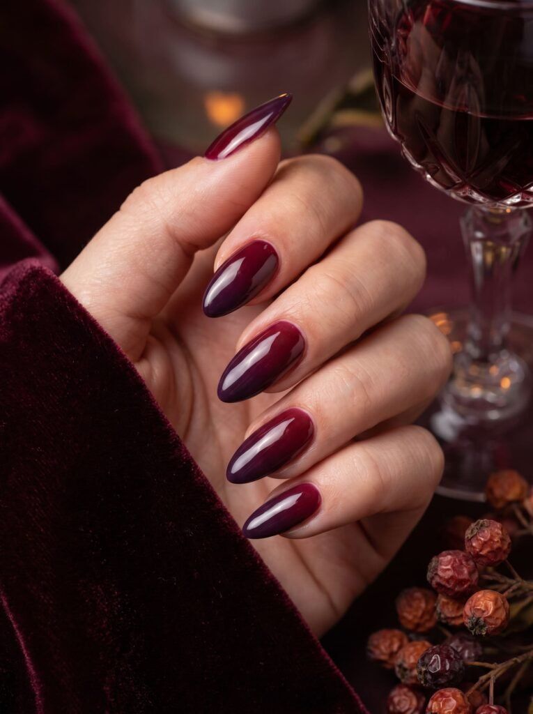 Burgundy almond nails holding a glass of red wine, deep wine gel set with velvet and berries