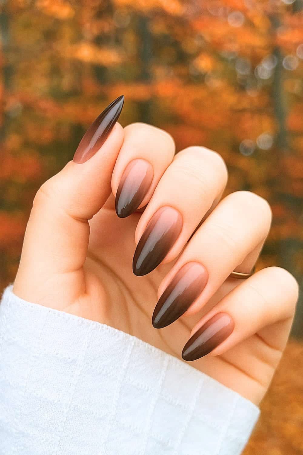 Chocolate ombre almond nails with autumn leaves in the background, brown gradient set