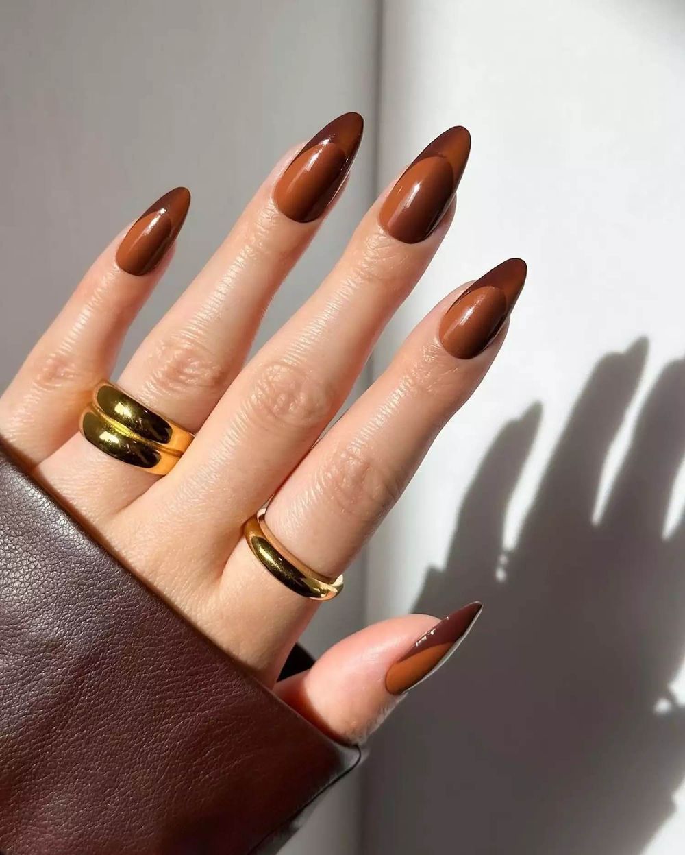 Glossy cognac brown almond nails with gold rings, warm amber brown gel set