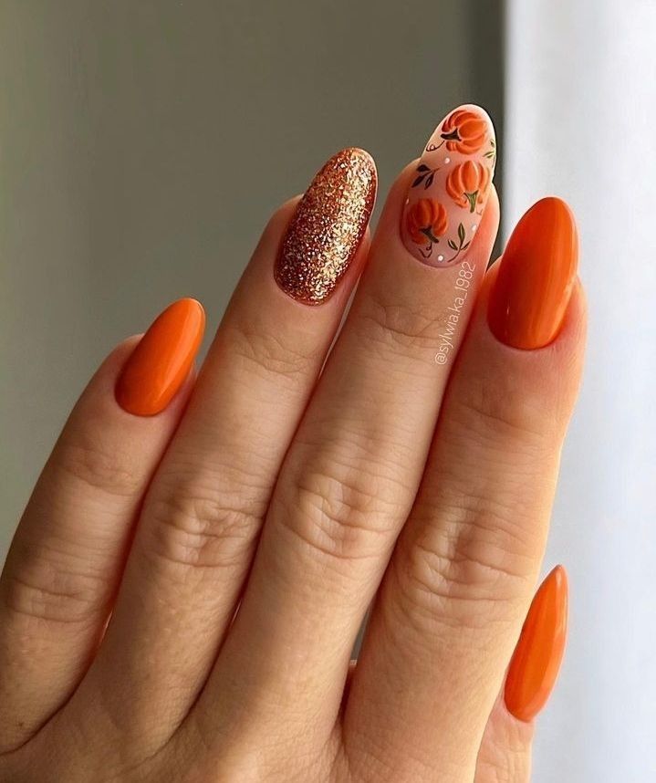 Orange almond nails with pumpkin art and a rose gold glitter accent nail