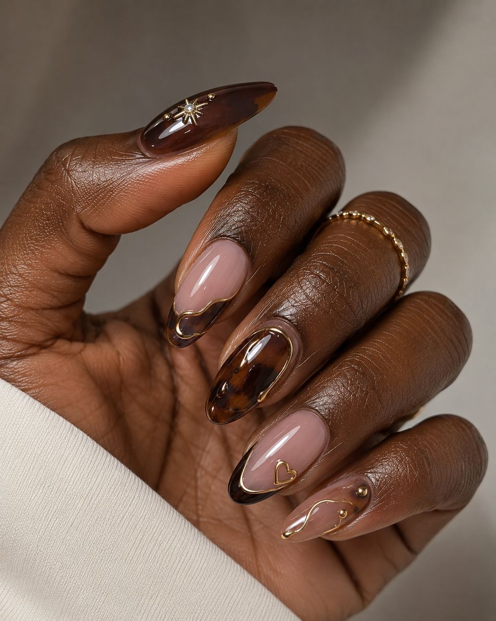 Tortoiseshell French almond nails on dark skin, amber and brown marbled tips with gold accents