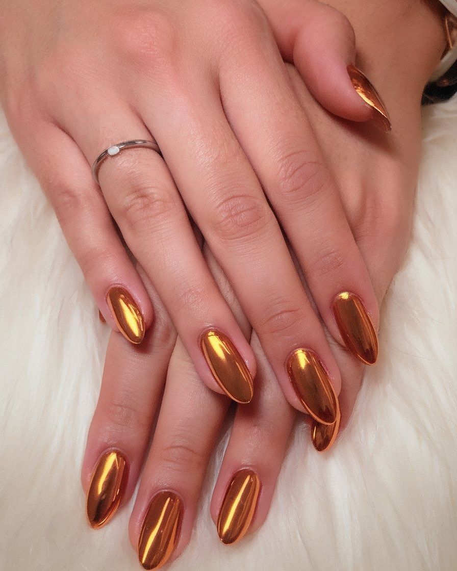 Gold chrome almond nails with a full mirror gold finish on hands resting on white fur