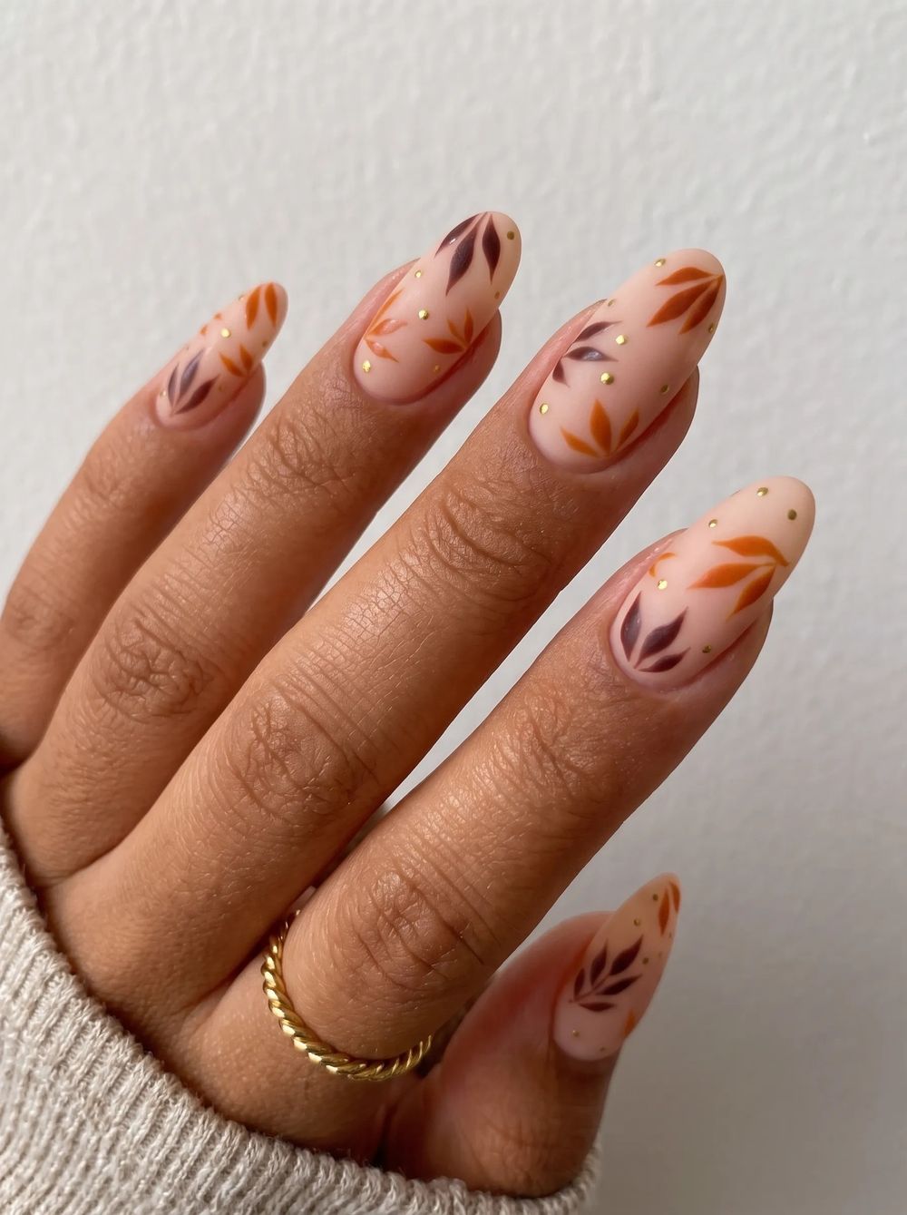 Nude nails with delicate leaf art in rust and gold on brown skin, sheer natural base almond set