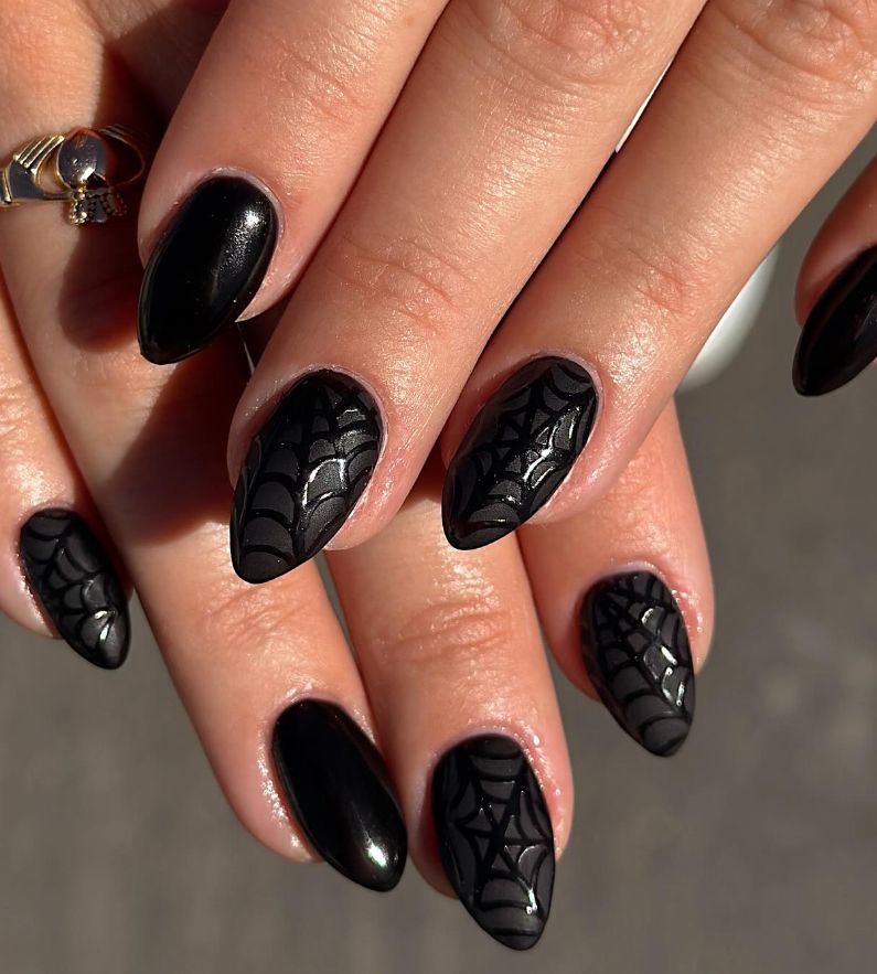 Glossy black almond nails with subtle tonal spiderweb art and a skull ring