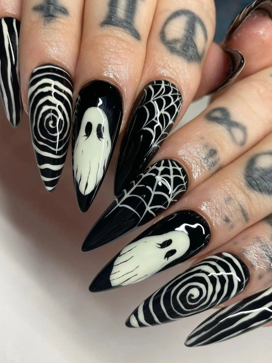 Black stiletto nails with white ghost and spiderweb art on a tattooed hand