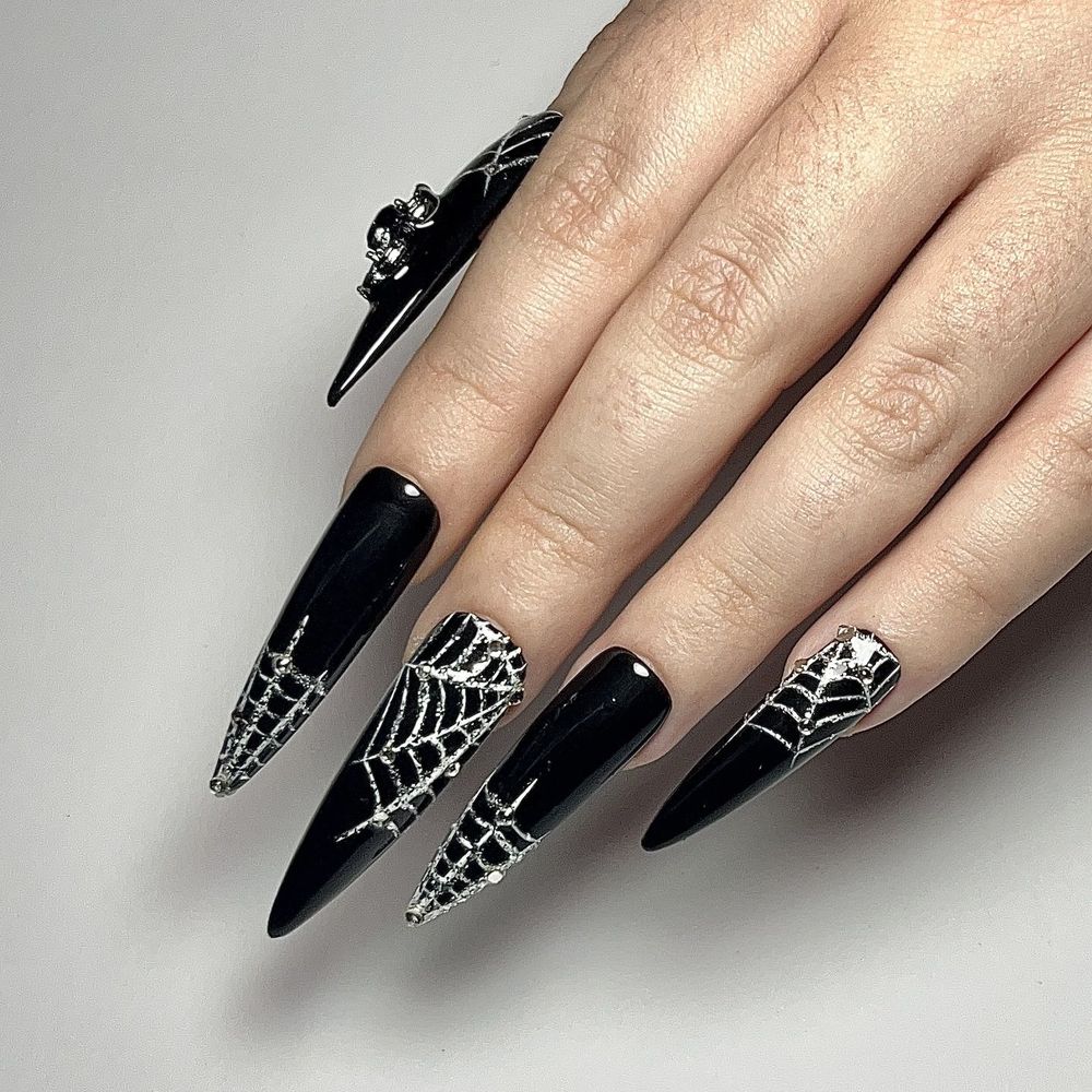 Glossy black stiletto nails with fine silver spiderweb art and a spider ring accent