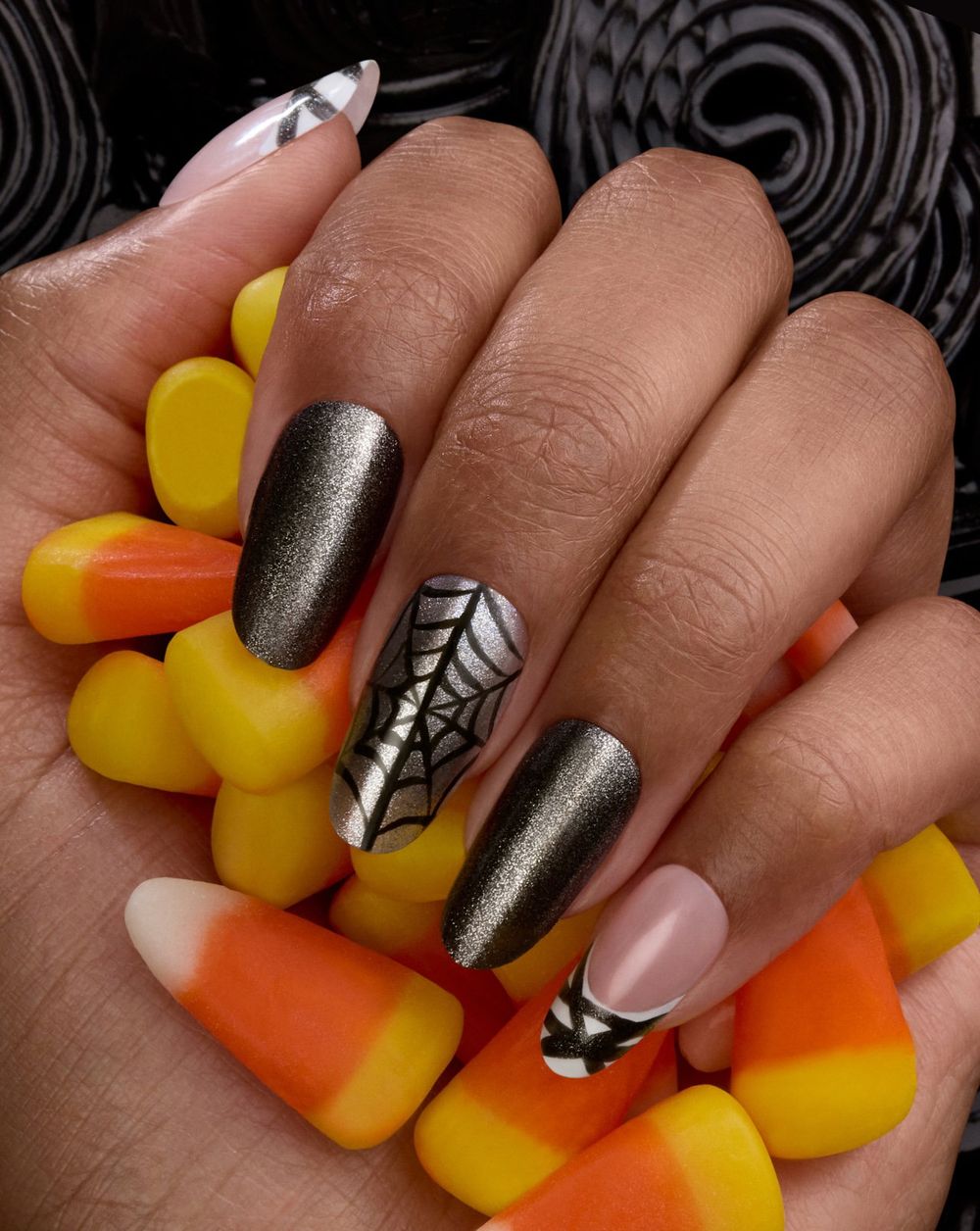 Metallic grey almond nails with a black spiderweb accent, hand holding candy corn