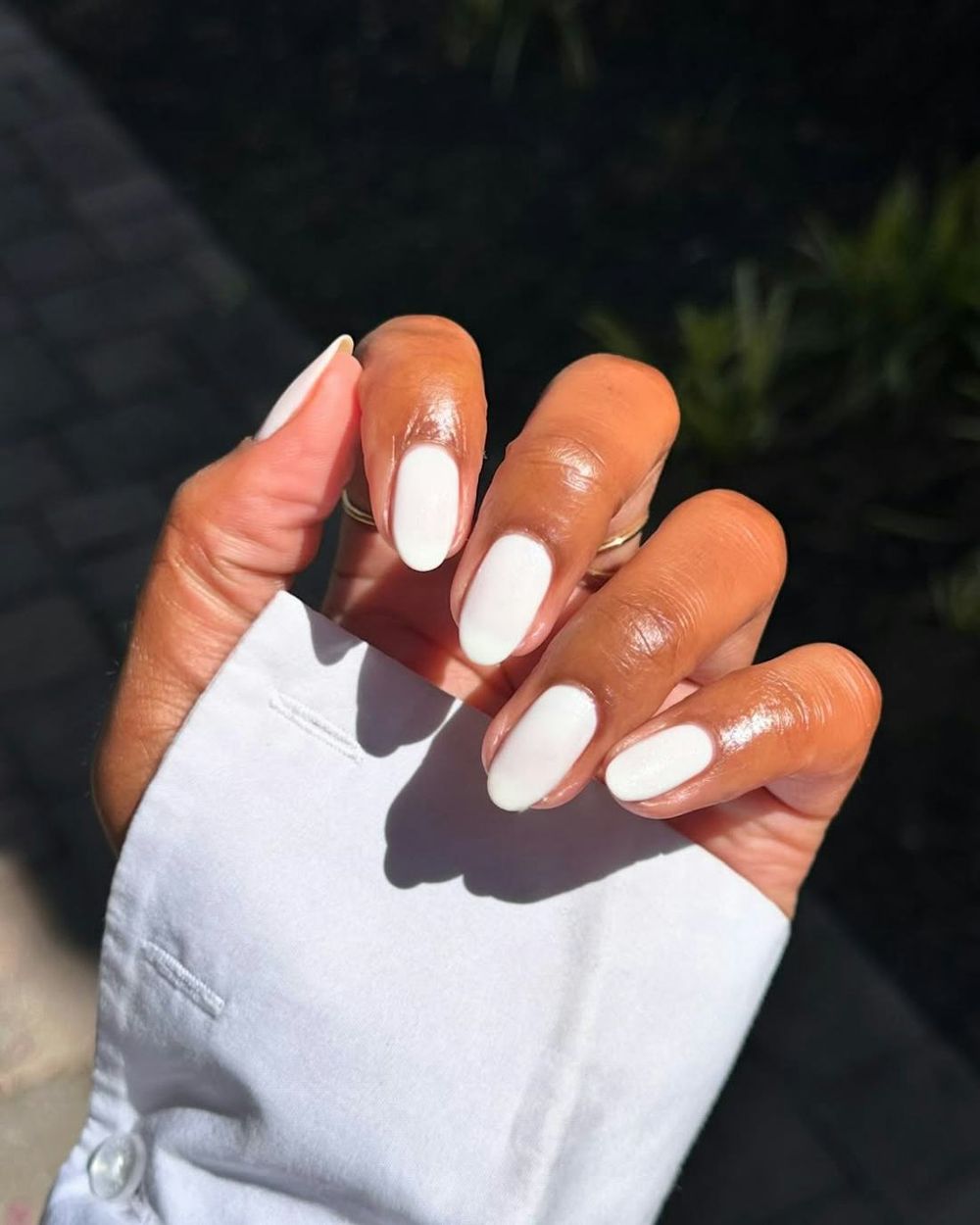 Glossy white almond nails on deep skin in sunlight, bright white glow outdoors