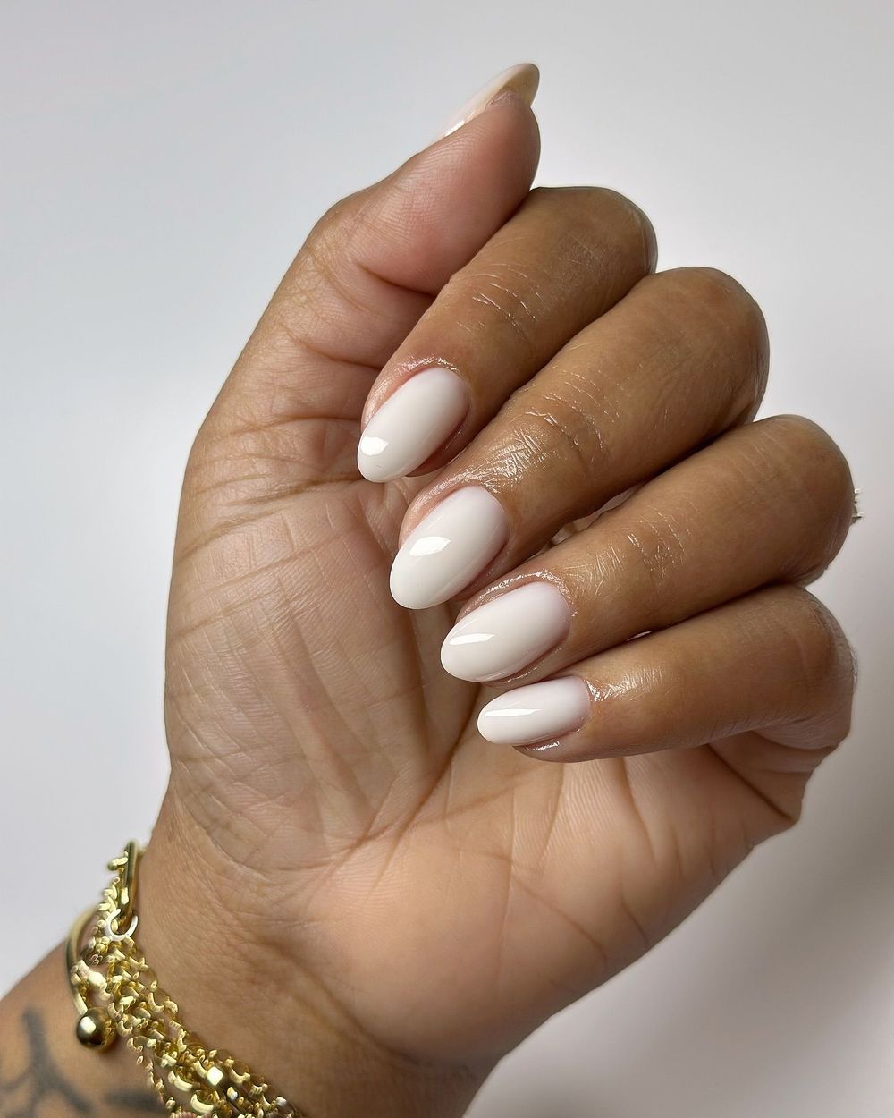 Ivory milky almond nails on brown skin with a gold bracelet, warm ivory glazed set