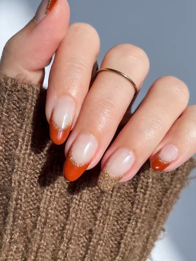 Orange French almond nails with gold glitter in a knit, orange tips with glitter accents