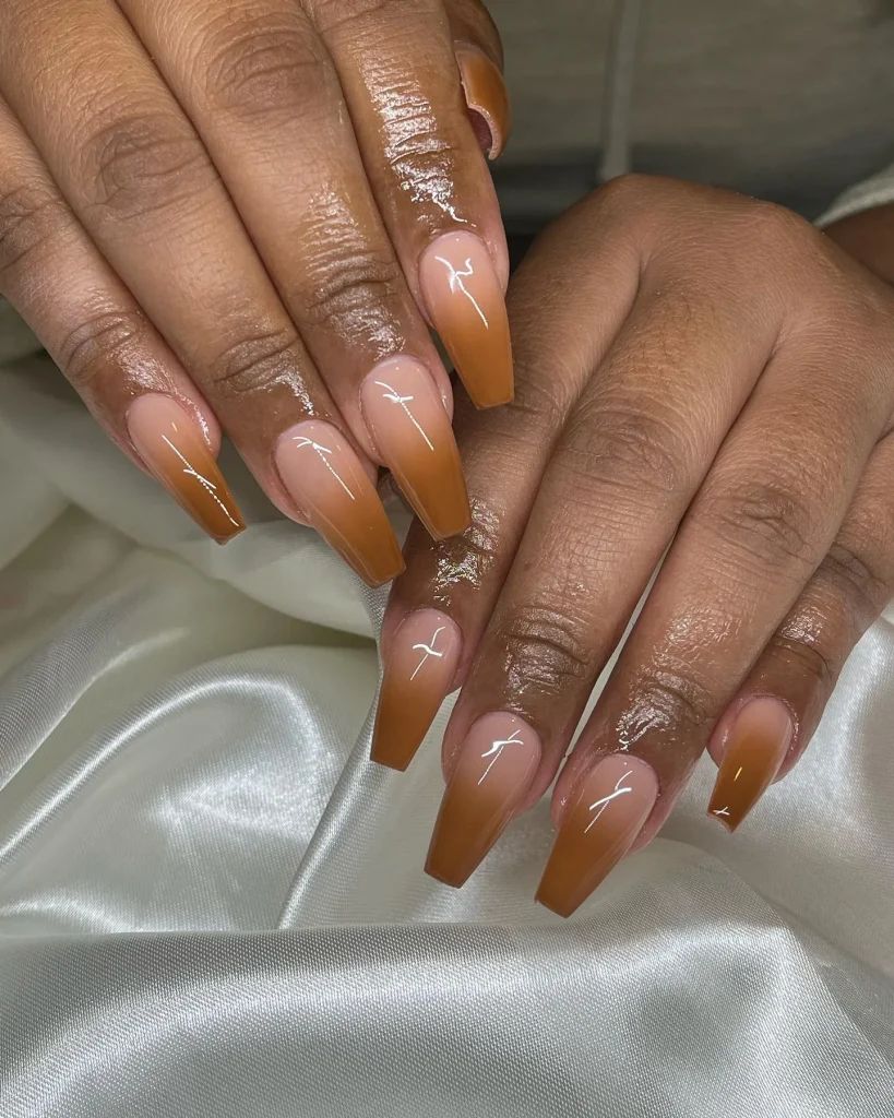 Caramel ombre coffin nails on dark skin over white silk, glossy gradient from nude to caramel