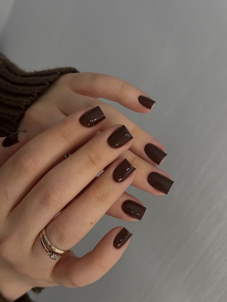 Short chocolate brown square nails on two hands in knit sweaters, a matching pair of fall manicures