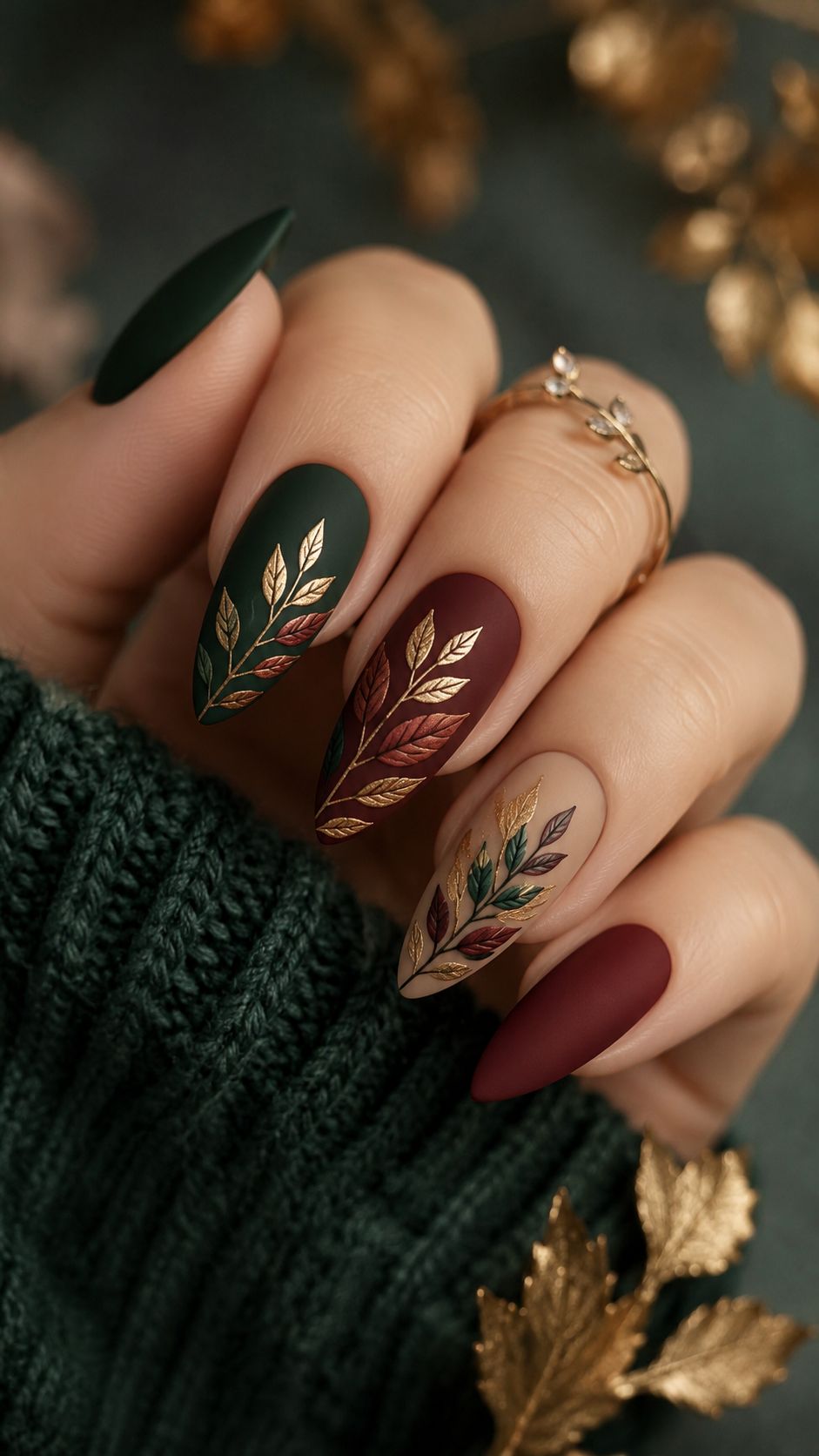 Forest green nails with hand painted leaf art and gold accents on a dark green set in a knit sweater