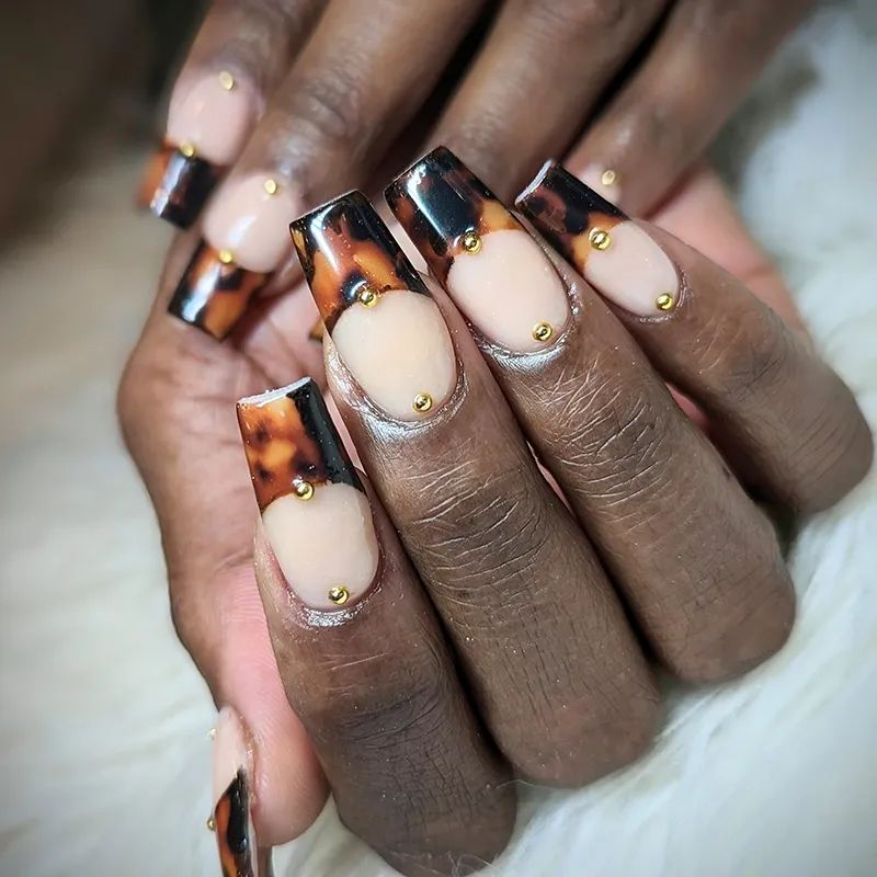 Black French coffin nails with a tortoiseshell accent on dark skin, black tips and one marble nail