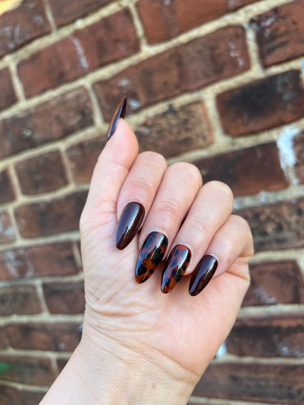 Dark tortoiseshell almond nails by a brick wall, deep amber marble in daylight