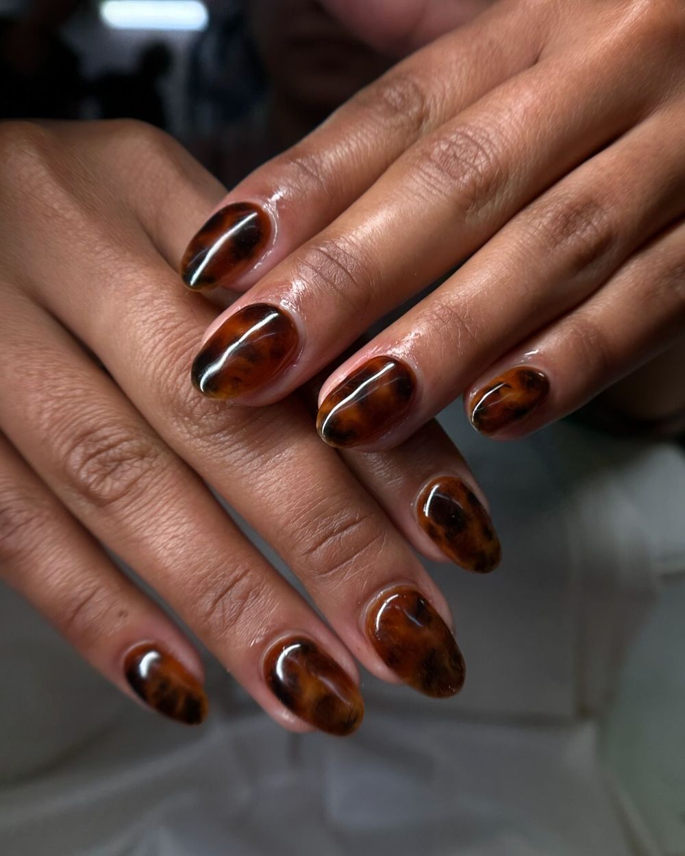 Dark tortoiseshell almond nails on brown skin, deep amber marble almond set