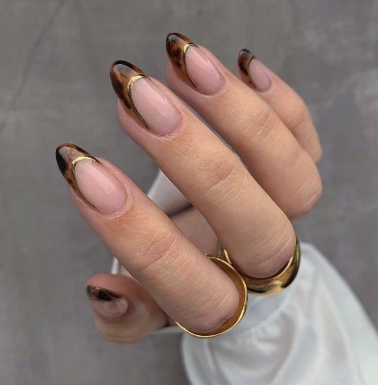 Nude almond nails with a gold band and tortoiseshell French, gold line above tortoise tips