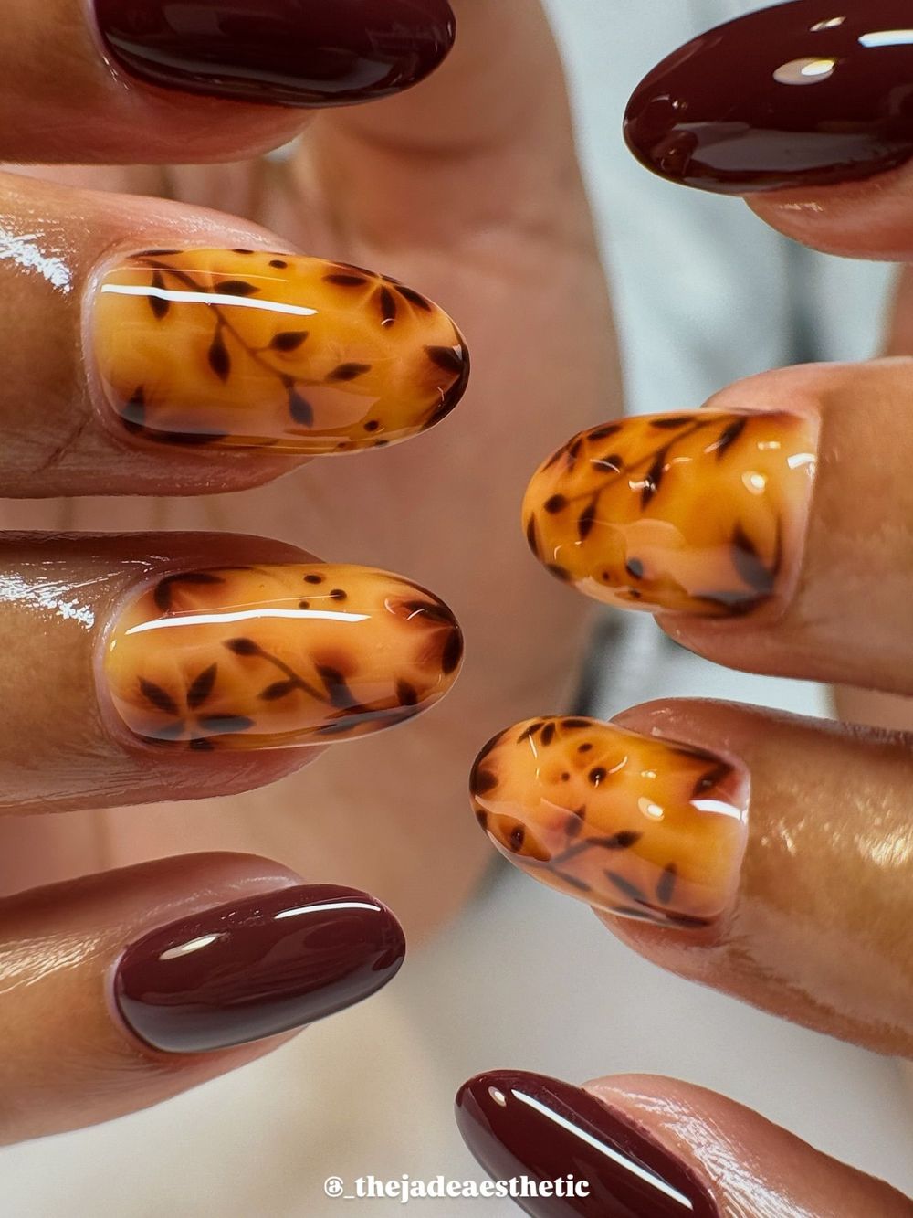 Tortoiseshell and burgundy almond nails close up, amber marble next to deep red gloss