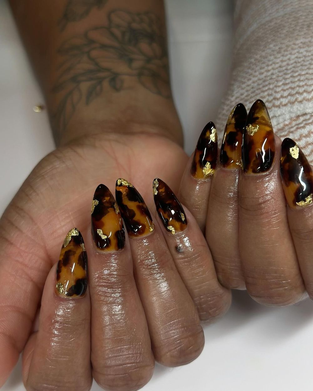 Tortoiseshell stiletto nails with gold foil on dark skin, long amber marble with gold